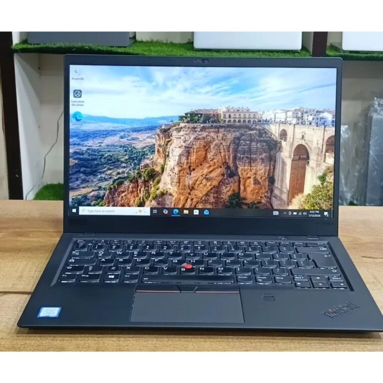 Matte black Lenovo ThinkPad X1 Carbon laptop open on an executive desk showing the iconic red TrackPoint.